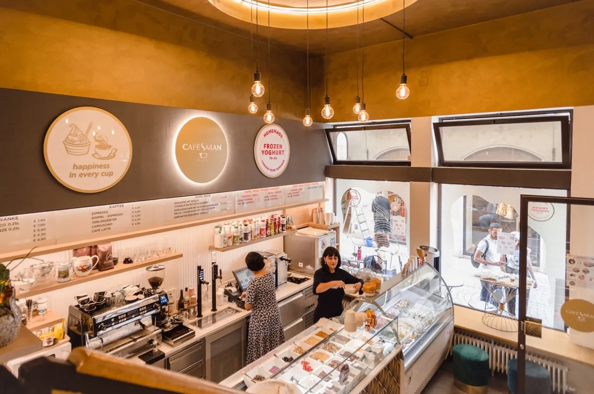Blick von oben in den Gastraum: goldene Decke, runde Leuchtschilder mit Logo, Theke mit Kaffeemaschine